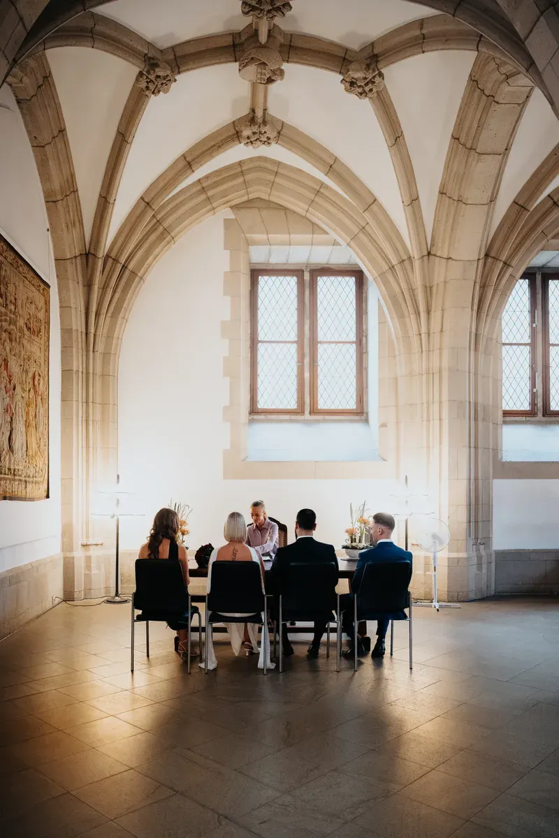 Blick von hinten auf Braut, Bräutigam und Trauzeugen vor dem Standesbeamten in der Rentkammer