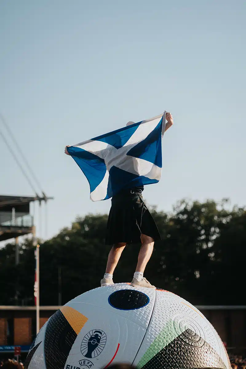 Ein Schotte mit Flagge steht auf einem EM-Ball.