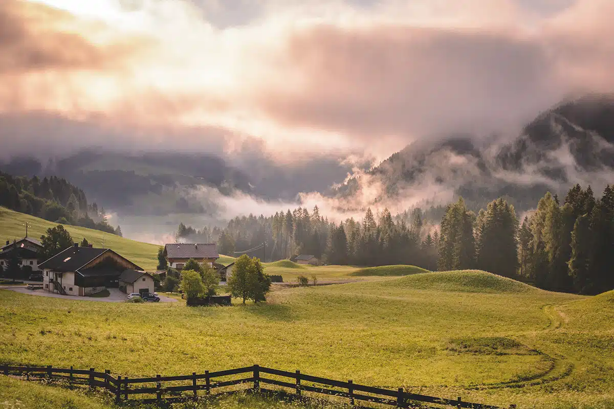 Grüne Landschaft mit Bergen im Hintergrund. Die Sonne scheint und es ist nebelig.