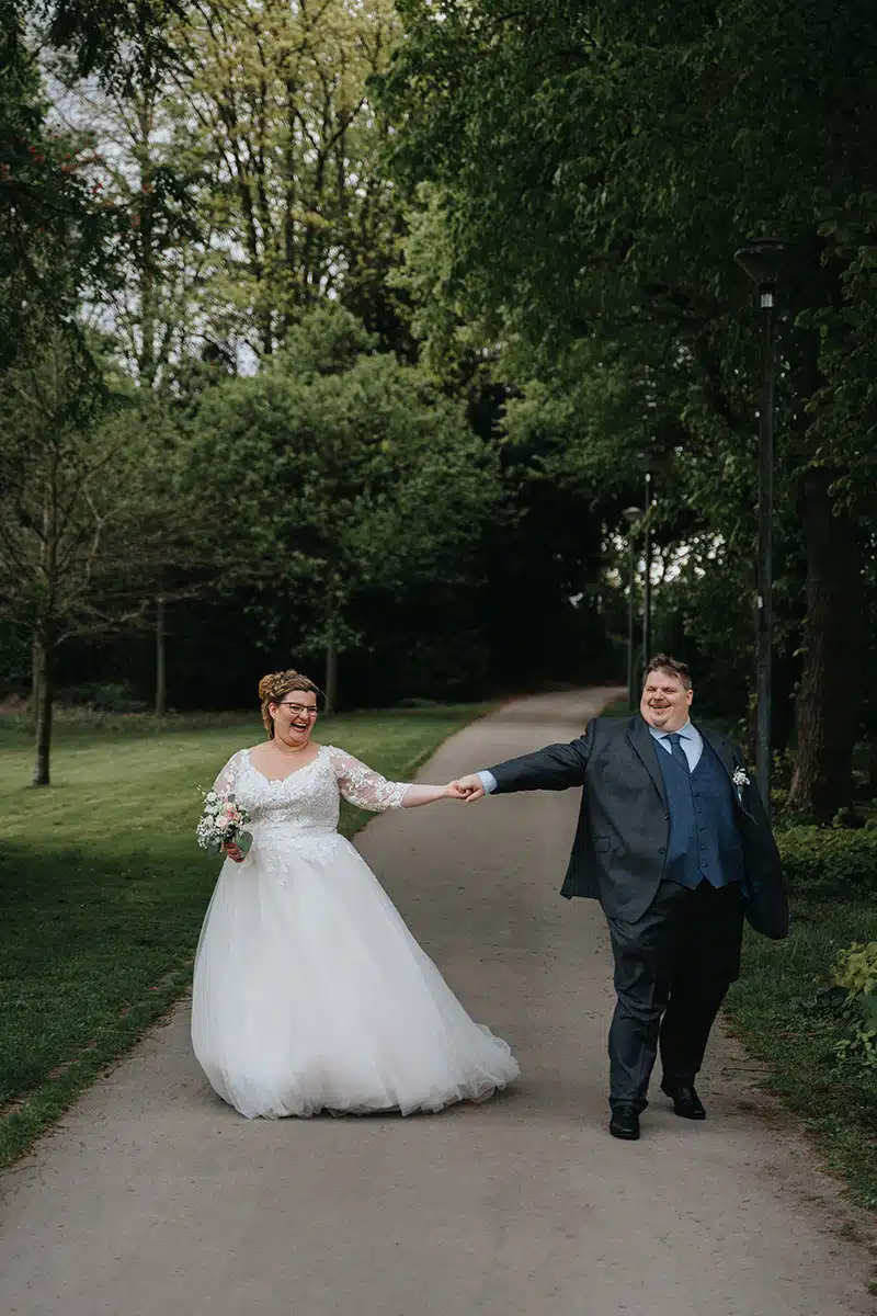 Ein Hochzeitspaar läuft Hand in Hand in einem Parkt in Essen, SChloss Borbeck.