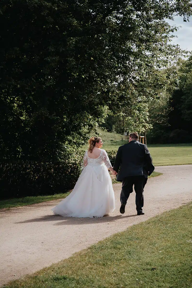 Ein Hochzeitspaar läuft Hand in Hand in einem Parkt in Essen, SChloss Borbeck.