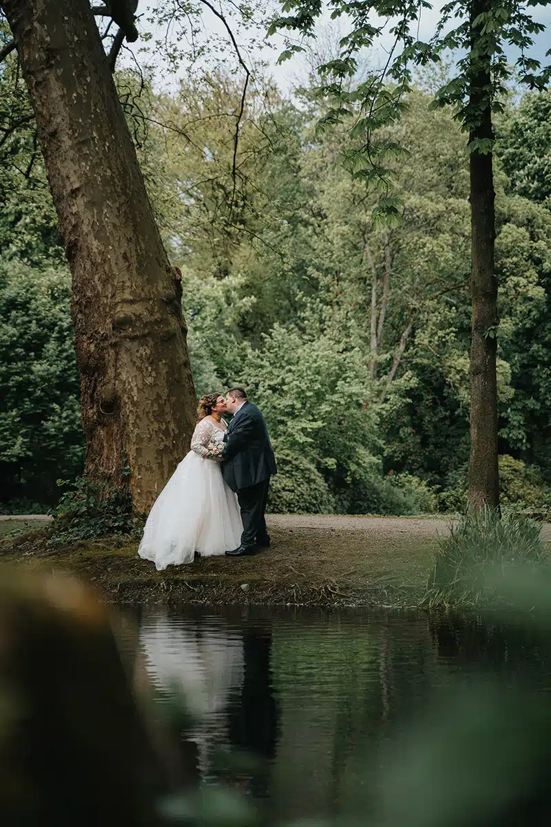 Ein Hochzeitspaar steht sich gegenüber an einem Teich in einem Parkt in Essen, SChloss Borbeck.