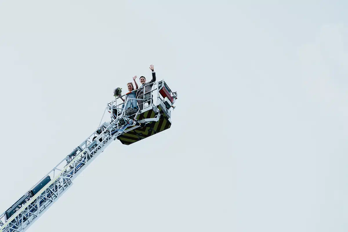 Braut und Bräutigam stehen im Korb einer Drehleiter der Freiwilligen Feuerwehr Sankt Augustin und winkt.