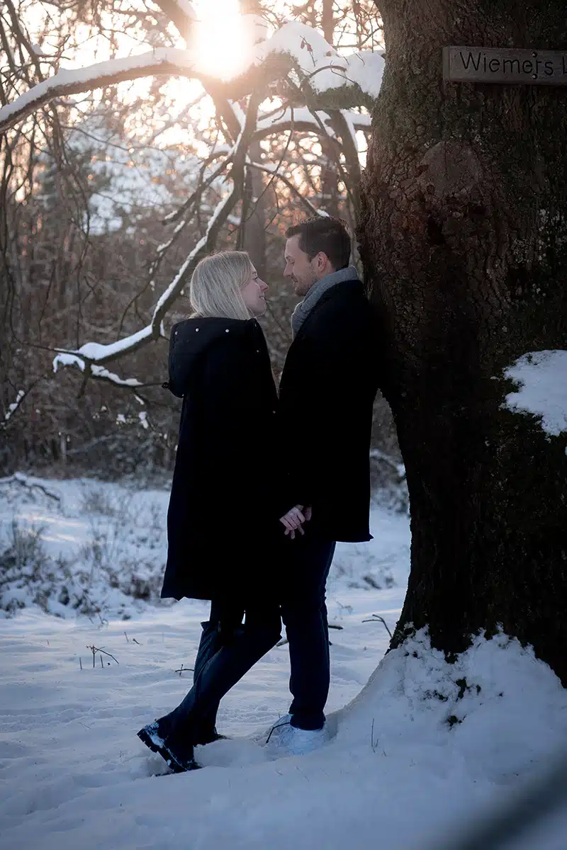 Ein Paar steht in winterlicher Landschaft in der Wahner Heide an einen Baum gelehnt.