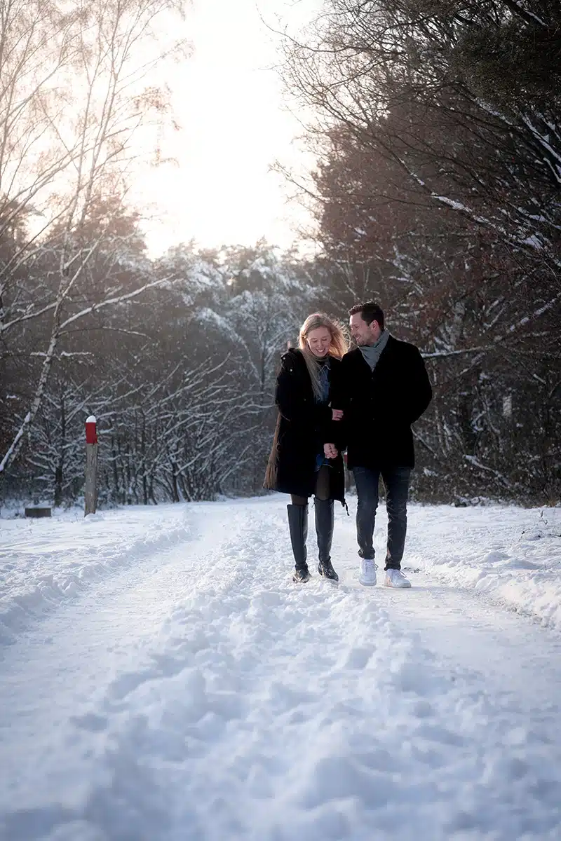 Ein paar läuft Hand in Hand durch eine winterliche Landschaft der Wahner Heide.