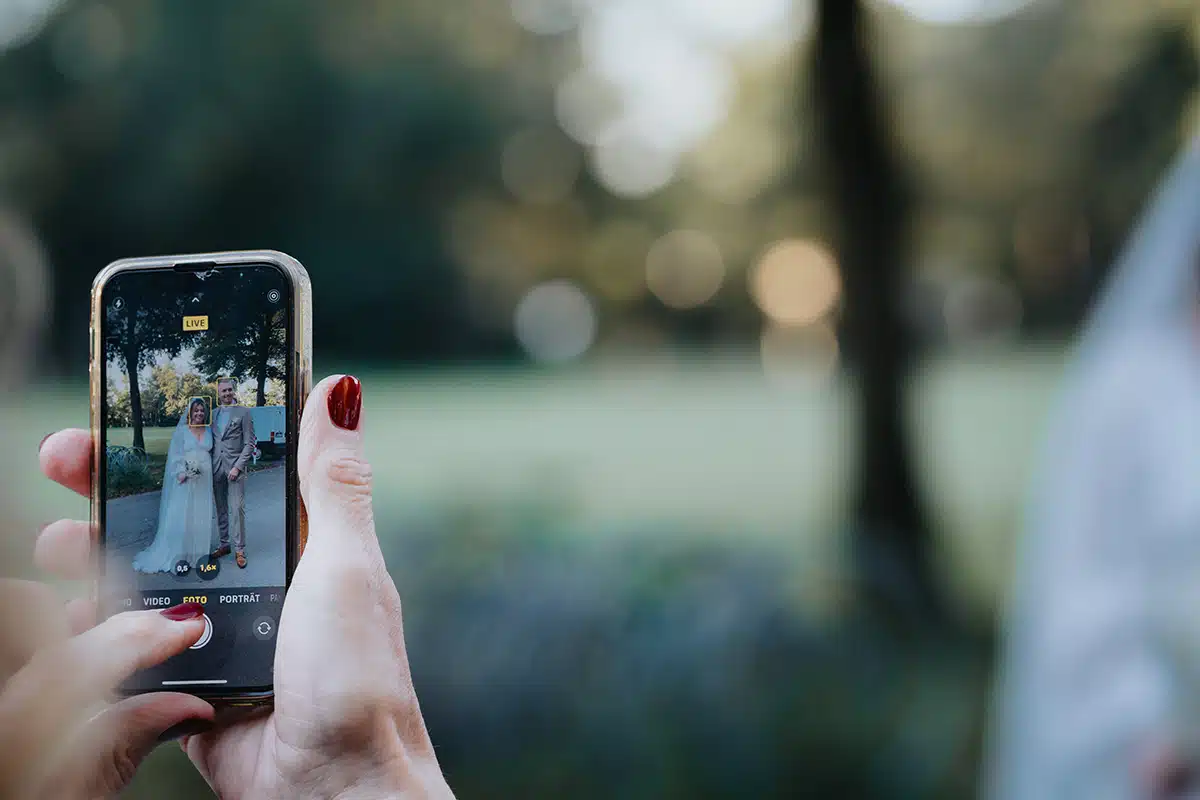 Jemand fotografiert das Hochzeitspaar mit dem Smartphone.