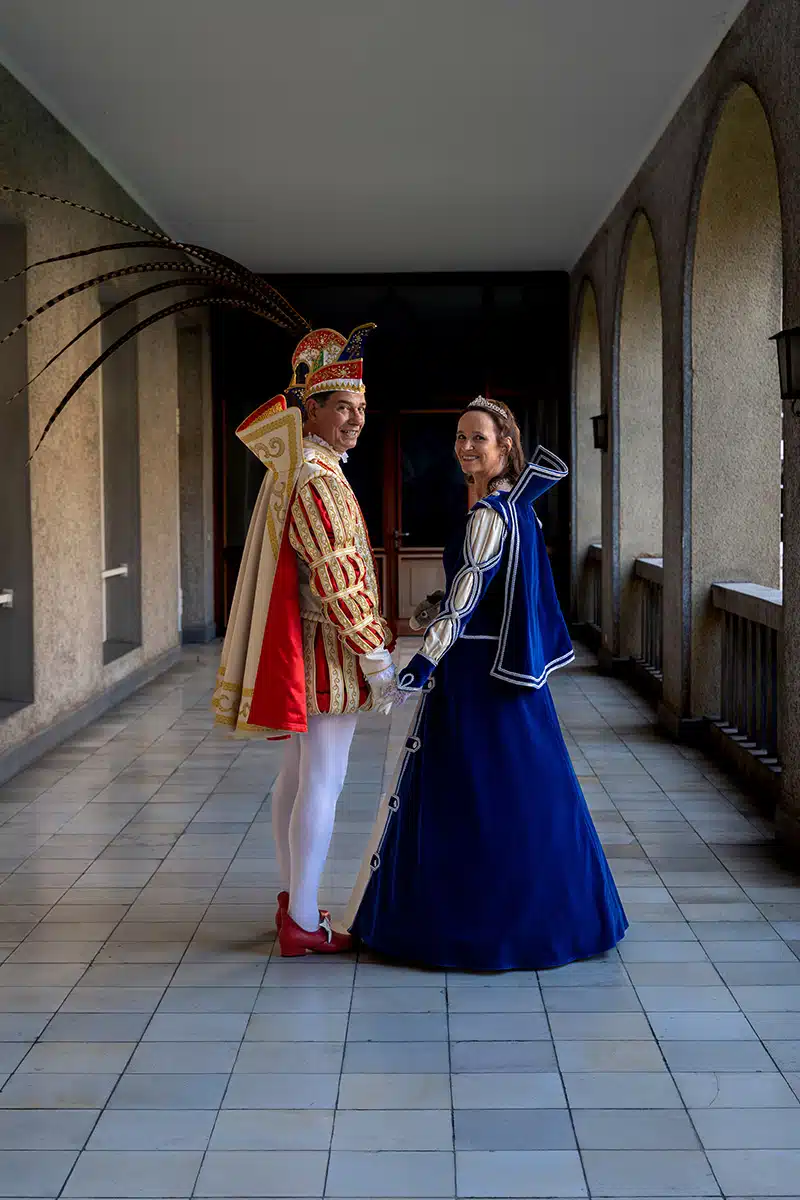 Das Sankt Augustiner Prinzenpaar 2023/2024 läuft Hand in Hand einen Gang entlang und schaut dabei in die Kamera.