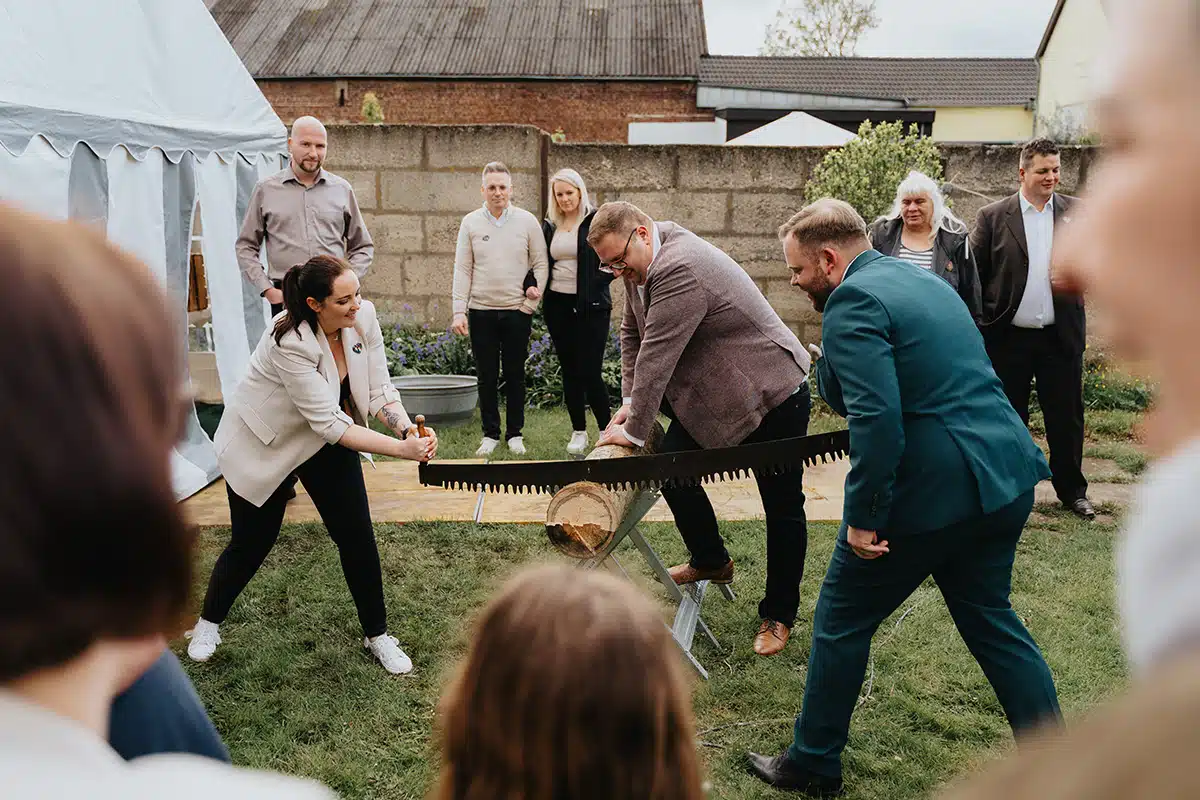 Braut und Bräutigam beim zersägen eines Baumstamms.