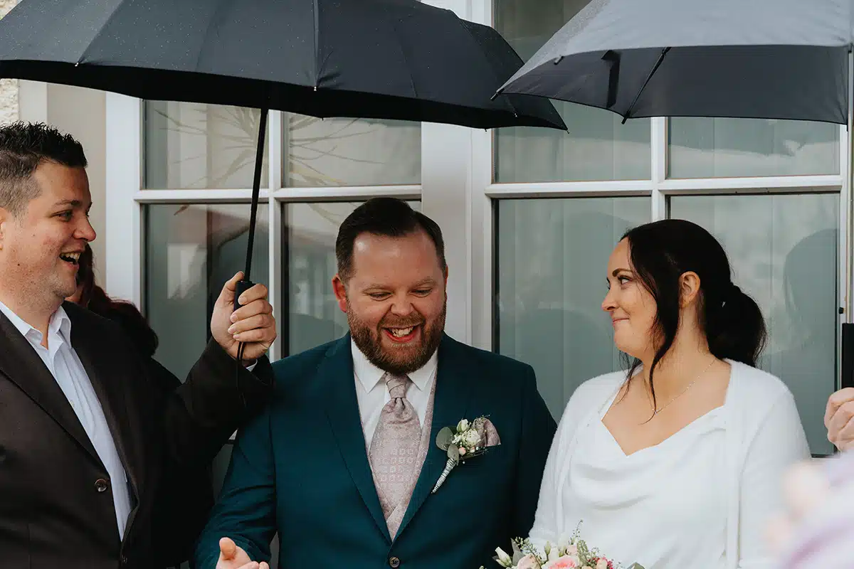 Braut und Bräutigam stehen unter Regenschirmen.