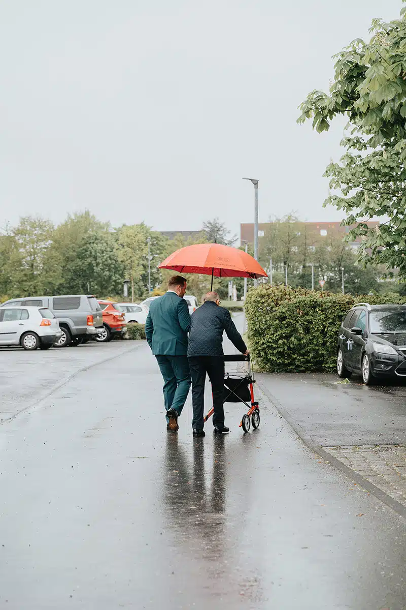 Der Bräutigam begleitet seinen Großvater mit einem Schirm.