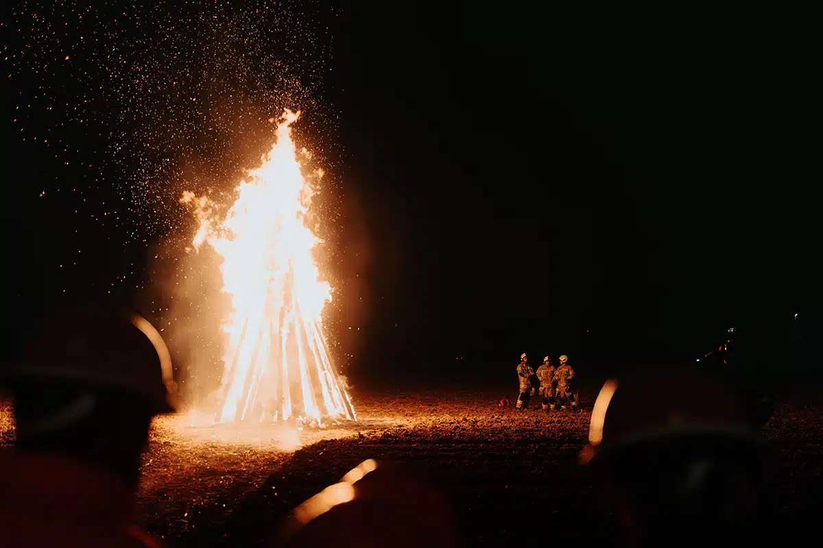 Das große Martinsfeuer brennt hell beim Martinszug Sankt Augustin Niederpleis 2024. Eine Gruppe Menschen schaut dabei zu.