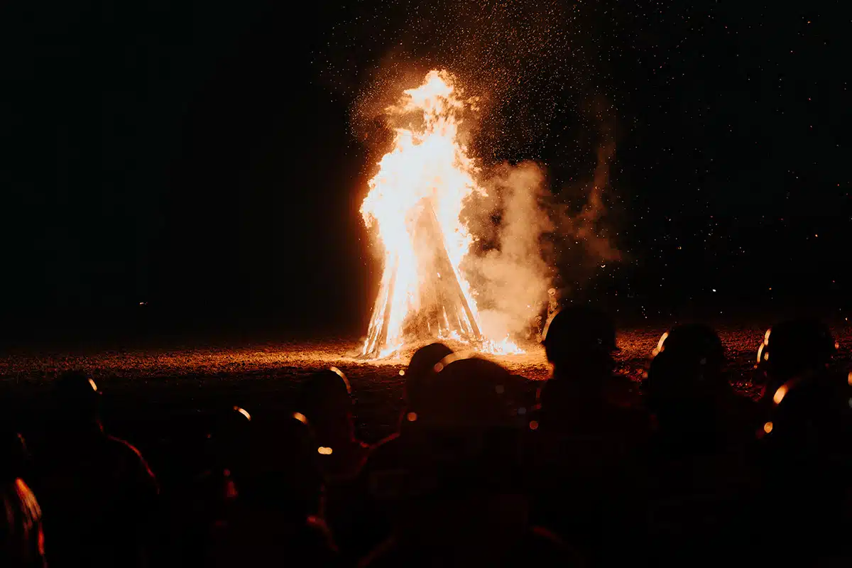 Das große Martinsfeuer brennt hell beim Martinszug Sankt Augustin Niederpleis 2024. Eine Gruppe Menschen schaut dabei zu.