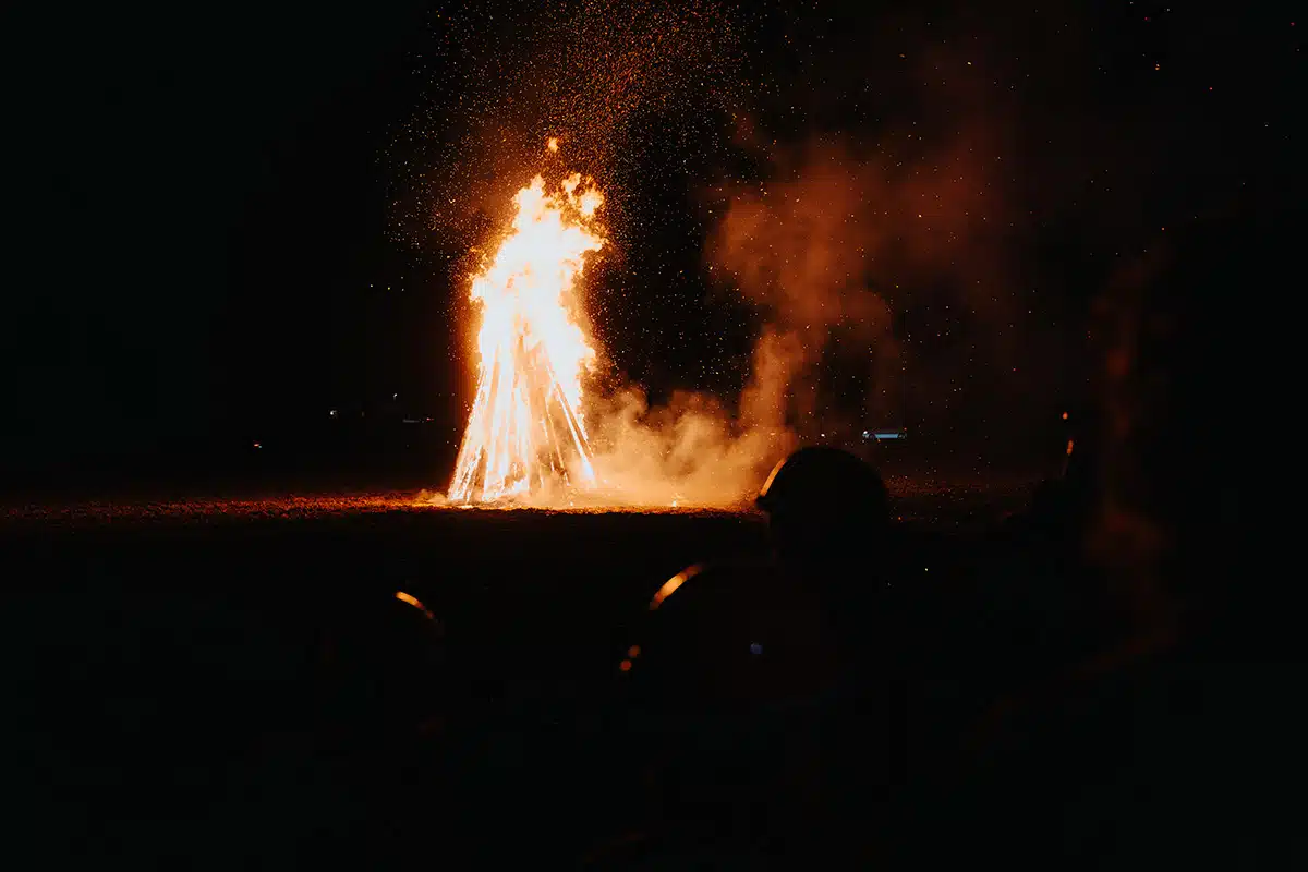 Das große Martinsfeuer brennt hell beim Martinszug Sankt Augustin Niederpleis 2024. Eine Gruppe Menschen schaut dabei zu.