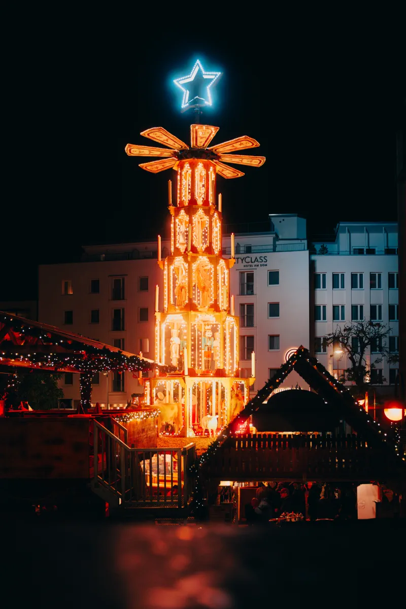 Eine große, beleuchtete Weihnachtspyramide im Weihnachtsdort auf dem Weihnachtsmarkt am Kölner Dom.