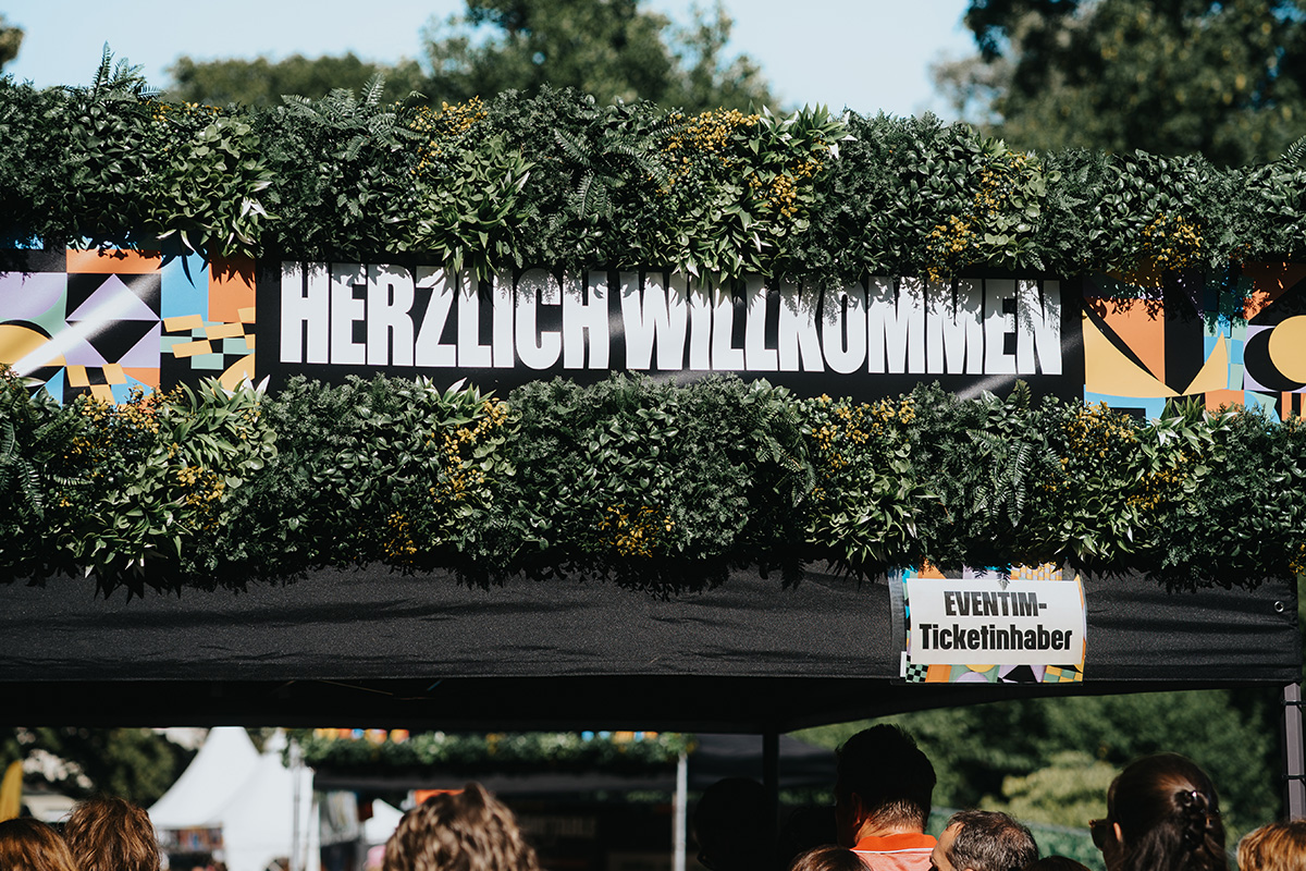 Grün geschmückter Eingangsbereich mit ‚Herzlich Willkommen‘-Schild beim Querbeat Festival Randale & Freunde 2025