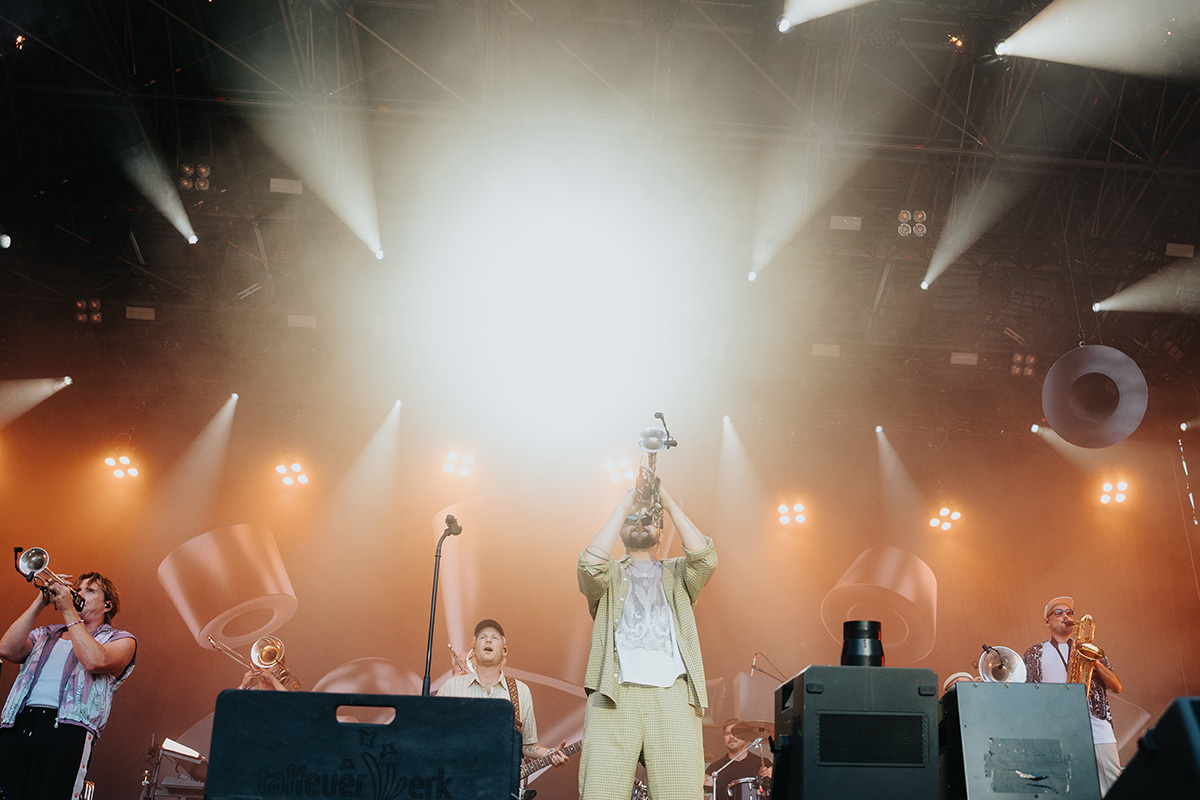 Querbeat auf der Bühne des Festivals Bonn 2025 – Trompeter zentral im Spotlight, begleitet von Bandmitgliedern mit Blasinstrumenten und dramatischer Bühnenbeleuchtung. Fotografiert von Philipp Wildfeuer