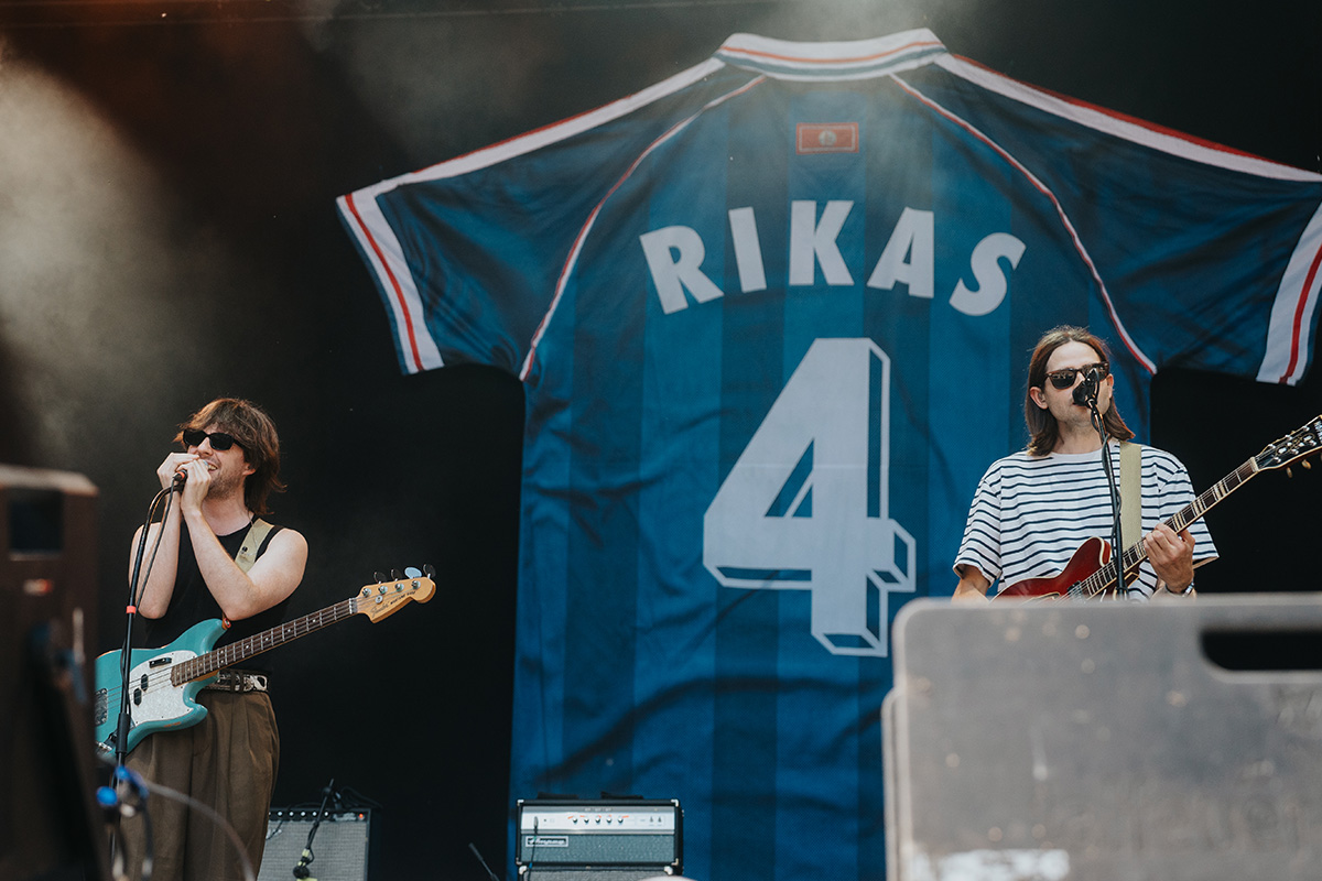 Zwei Musiker der Band RIKAS auf der Bühne beim Querbeat Festival Bonn 2025, mit großem blauem Trikot im Hintergrund – Freunde & Randale 2025. Fotografiert von Philipp Wildfeuer