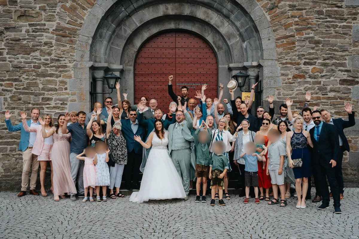 Die Hochzeitsgäste machen ein Gruppenbild vor der Kirche; festgehalten von Hochzeitsfotograf Philipp Wildfeuer.